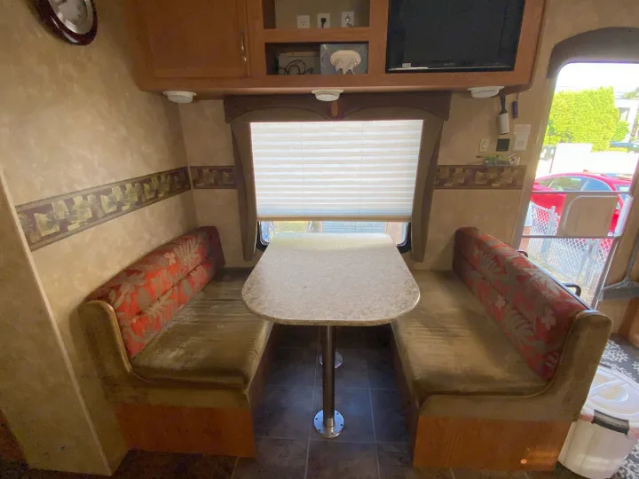 RV rental dinette setup with a speckled table, olive benches, and red patterned backrests. Overhead cabinets & window blinds visible.. Jayco Jay Flight G2 2008