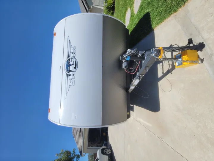 Front of a white Shasta travel trailer, an ideal rv rental, parked on a driveway, showing its hitch against blue sky.. Forest River Shasta 2021