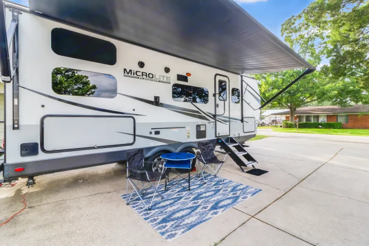 This RV rental features a white travel trailer with an extended awning, outdoor chairs, and a table set up on a driveway.. Forest River Flagstaff Micro Lite 2022