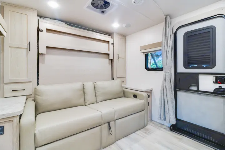 Experience comfort in this modern rv rental interior, featuring a cozy sofa, fold-down Murphy bed, and light wood finishes.. Forest River Flagstaff Micro Lite 2022