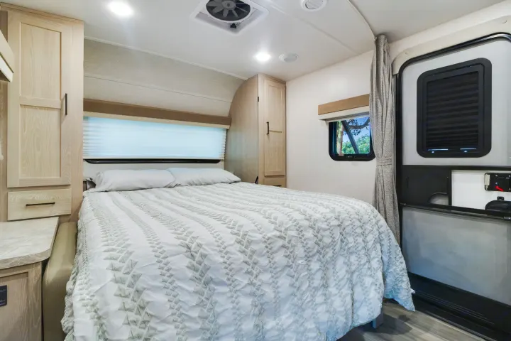 Step into comfort: a cozy RV rental bedroom featuring a full bed, light wood cabinetry, and window with outdoor view.. Forest River Flagstaff Micro Lite 2022