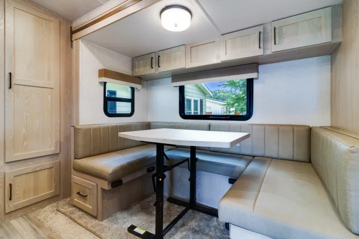 This RV rental interior features a cozy dinette with light wood finishes, comfortable seating, overhead storage, and windows.. Forest River Flagstaff Micro Lite 2022