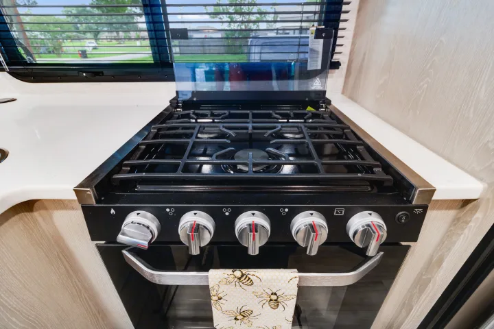 Experience RV rental comfort: a clean kitchen with a black gas stove, oven, and a charming bee-patterned towel.. Forest River Flagstaff Micro Lite 2022