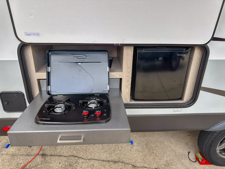 RV rental's outdoor kitchen features a pull-out two-burner stove and Insignia refrigerator, ideal for convenient campsite cooking.. Forest River Flagstaff Micro Lite 2022