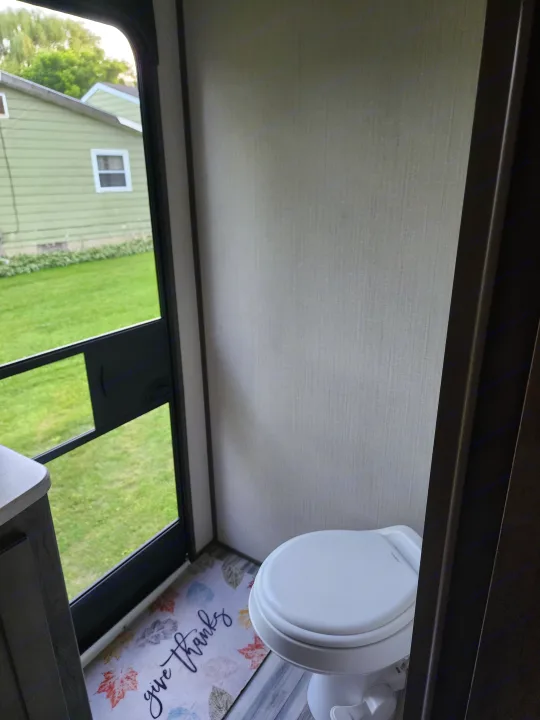 **RV rental** bathroom showcasing a toilet, screen door leading to a yard, and a "give thanks" floor mat.. Cruiser RV MPG Ultra Lite 2020