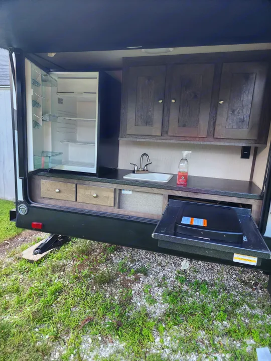This RV rental's outdoor kitchen features a convenient setup with an open fridge, sink, cabinets, and pull-out grill.. Cruiser RV MPG Ultra Lite 2020