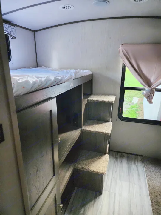 RV rental: interior with a top bunk bed, integrated storage, carpeted steps, and a window view of green outdoors.. Cruiser RV MPG Ultra Lite 2020