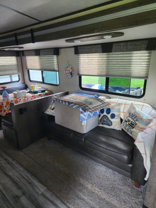 Inside a comfy rv rental, featuring a dark leather sofa with decorative pillows and a dining area with a colorful fruit tablecloth.. Cruiser RV MPG Ultra Lite 2020