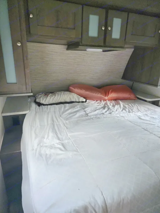 RV rental bedroom: a comfortable bed with pillows and white comforter, dark overhead cabinets, and side shelves.. Cruiser RV MPG Ultra Lite 2020