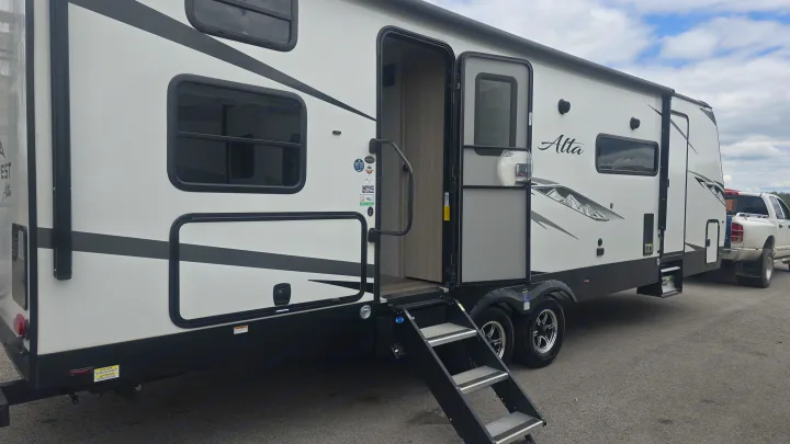 A large white Alta travel trailer for rv rental with its main door open and steps extended, parked outdoors.. East to West Alta 2022