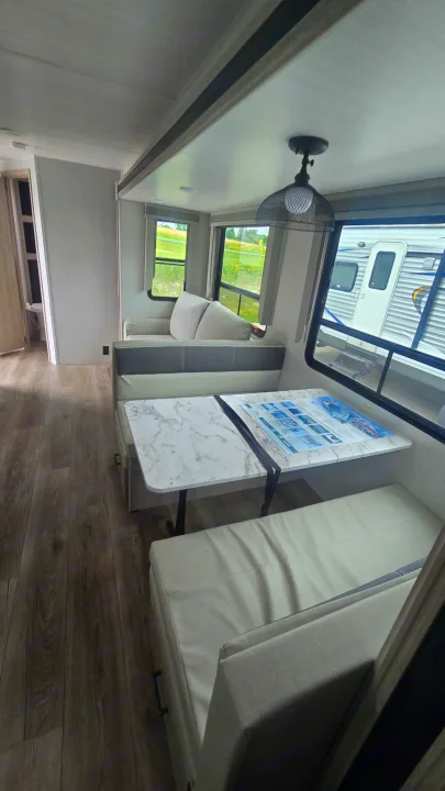 Inside this modern RV rental: a bright dinette with marble-look table, comfy bench, and a sofa in the living space.. East to West Alta 2022