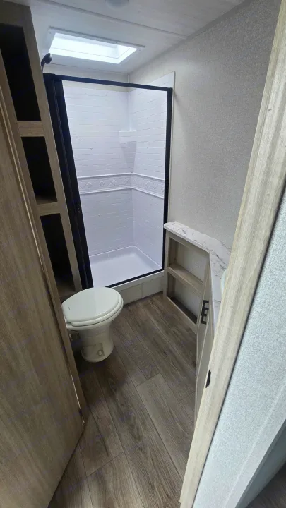 Modern RV rental bathroom with compact shower, white toilet, and built-in wood-look storage. Practical layout for travel.. East to West Alta 2022