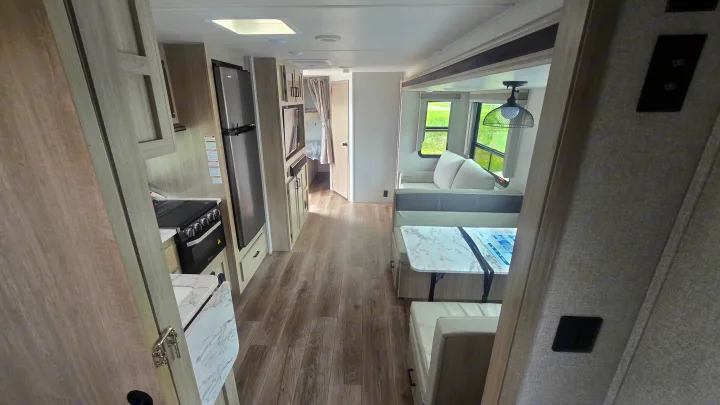 Modern RV rental interior showing kitchen, dinette, and living space with light wood tones and ample light.. East to West Alta 2022