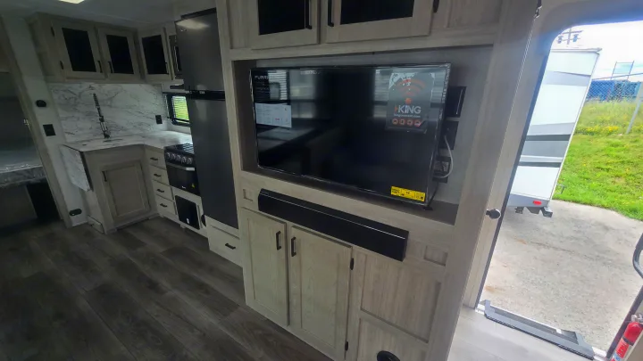 Spacious rv rental interior featuring a modern kitchen with marble-look counters, entertainment center, and light wood cabinetry.. East to West Alta 2022