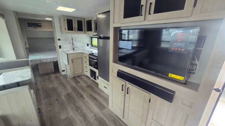Explore this modern RV rental interior featuring a well-equipped kitchen, entertainment center, and cozy bedroom.. East to West Alta 2022