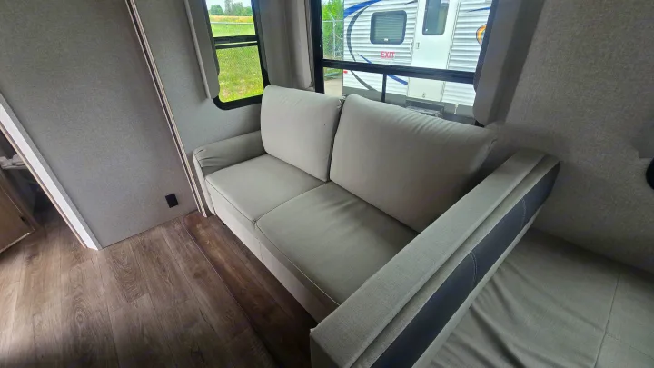 Comfortable light grey sofa inside an RV rental, with wood-look floor and views outside from the windows.. East to West Alta 2022