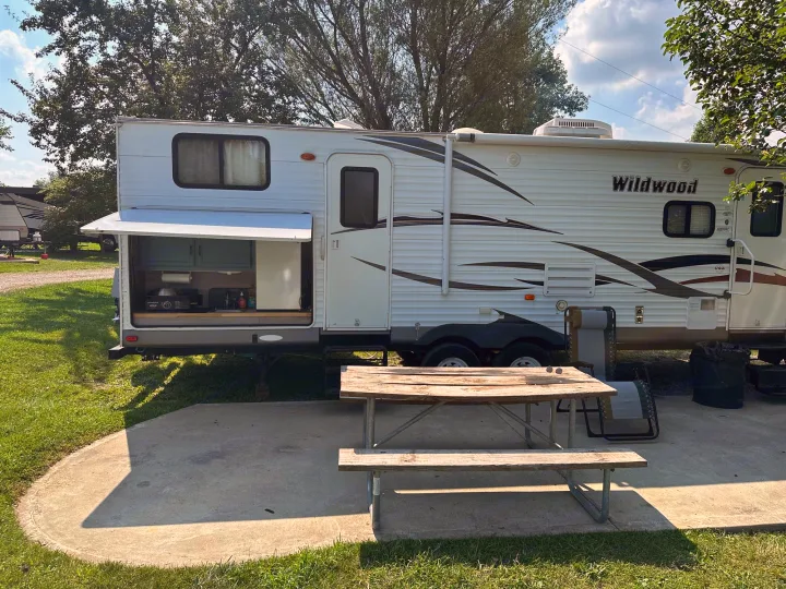 A travel trailer RV rental at a sunny campsite, complete with an outdoor kitchen and picnic table.. Forest River Wildwood 2012