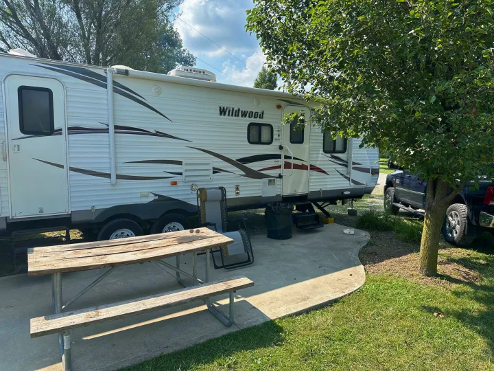 Spacious RV rental parked at a shady campsite with a picnic table, perfect for outdoor adventures.. Forest River Wildwood 2012
