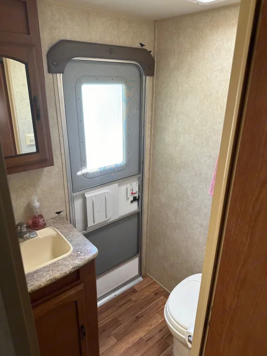Functional RV rental bathroom with sink, mirror, toilet, and exterior door. See details of this compact space for travel.. Forest River Wildwood 2012