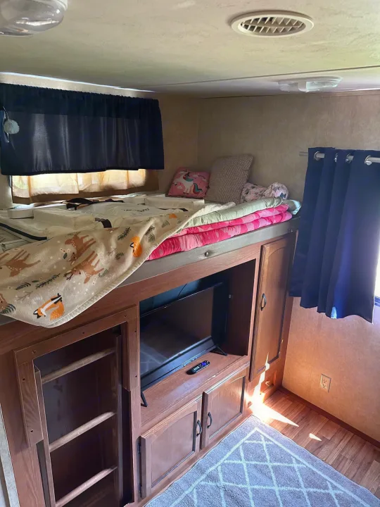 Inside an RV rental: a comfortable bunk bed with a TV, storage, and pull-out ladder for easy access.. Forest River Wildwood 2012