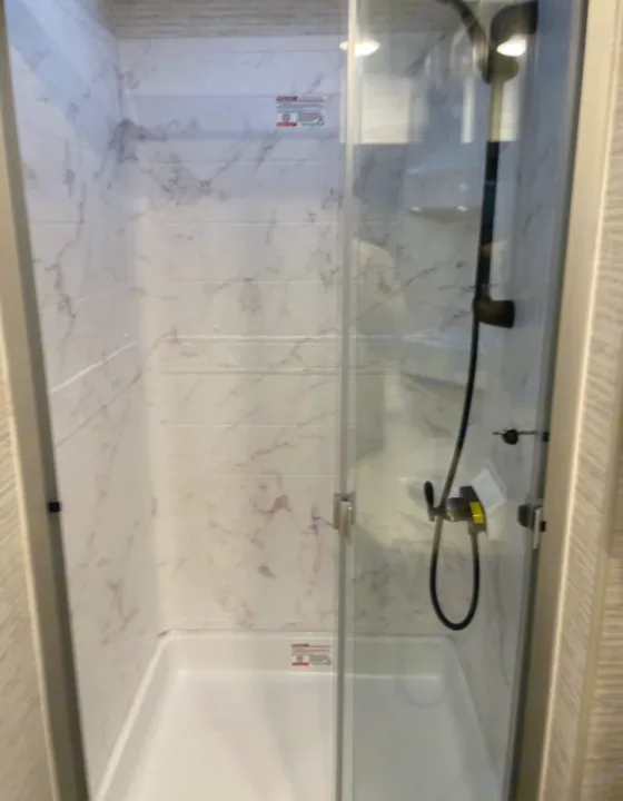 Clean RV rental shower featuring white marble-patterned walls, a glass door, and a black showerhead for comfortable travel.. Entegra Coach Other 2024