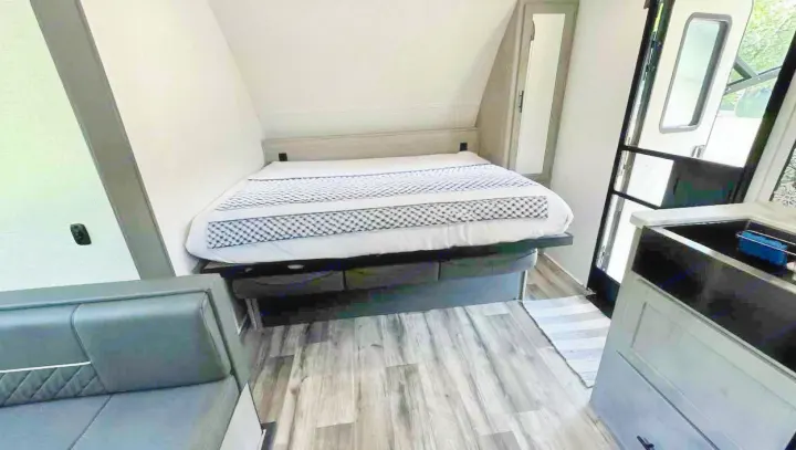 RV rental interior with comfortable bed, sleek couch, and kitchen sink. Wood-look flooring completes this cozy space.. Dutchmen Coleman Light 2023