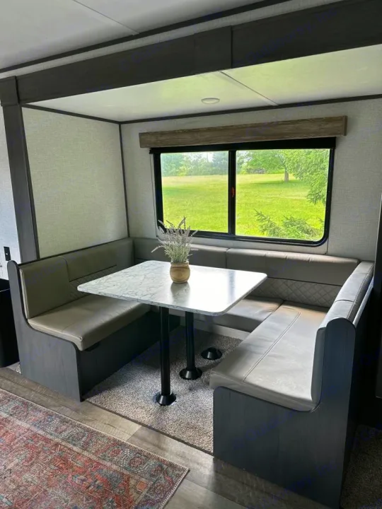 RV rental dinette features a U-shaped booth with light gray seating, marble-top table, and window view of a green field.. Aspen Trail LE 2022