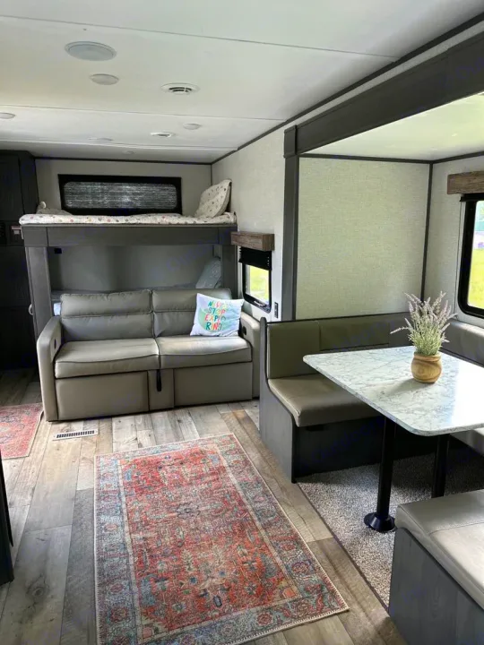 Inside an RV rental: bunk beds, sofa, dinette with table & plant. Light wood floors with a colorful rug.. Aspen Trail LE 2022