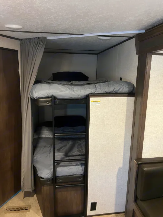 Inside an rv rental: a compact sleeping area with two neatly made bunk beds, ladder, and privacy curtain.. Dutchmen Coleman Lantern 2021