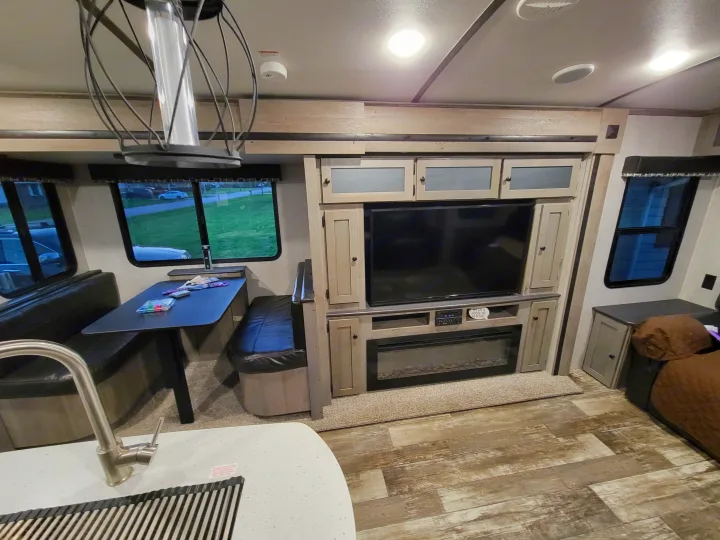 Modern RV rental interior with dinette, entertainment center, and kitchen sink, offering a bright and cozy travel space.. Keystone RV Outback 2019