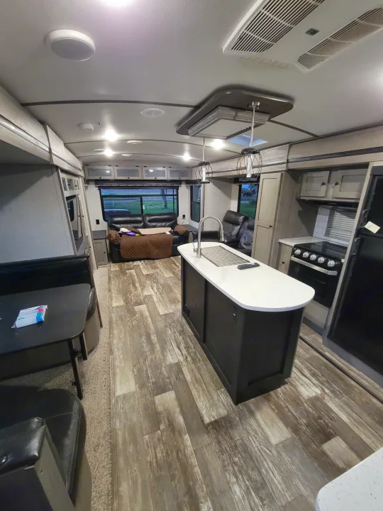 Modern RV rental interior with a fully equipped kitchen island, spacious living room, and dining area, ready for adventure.. Keystone RV Outback 2019