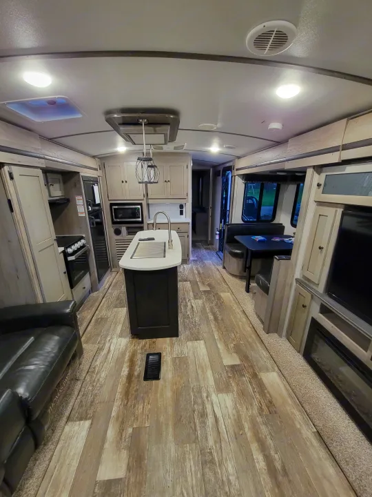 Bright RV rental interior: Full kitchen, dining booth, and living space with wood-look flooring and carpeted slide.. Keystone RV Outback 2019