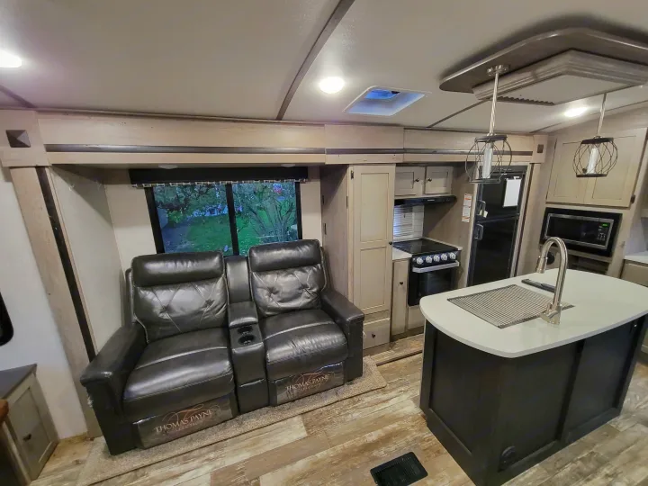 An inviting RV rental interior with comfy recliners, a well-equipped kitchen including stove and fridge, and island counter.. Keystone RV Outback 2019