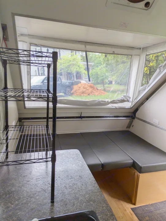 Inside an rv rental: functional camper living area with a bed, counter, and large windows revealing an outdoor scene.. A Liner A Liner Popup Trailer 2022