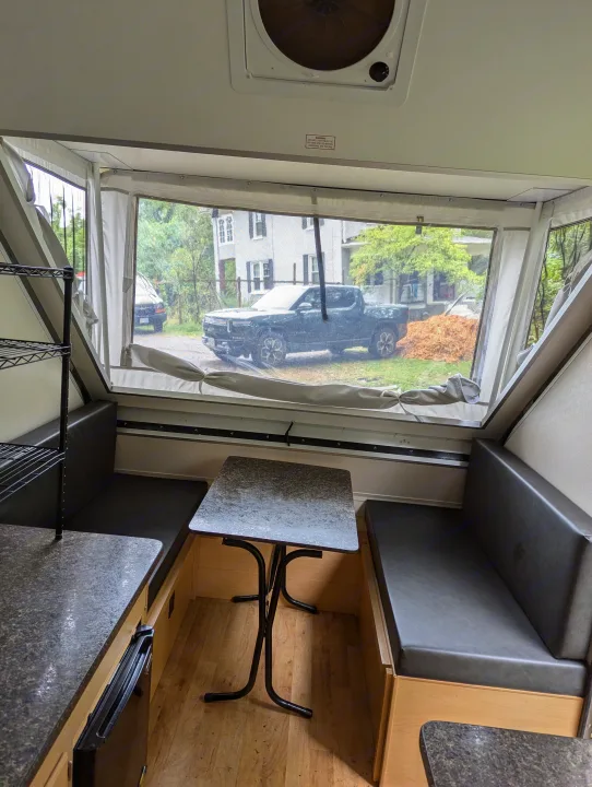 Inside an RV rental, this A-frame camper features a cozy dining area with a clear window view of a truck.. A Liner A Liner Popup Trailer 2022