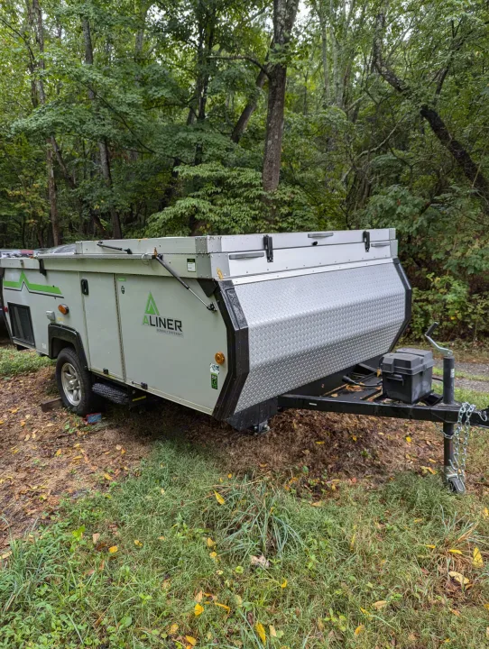 An Aliner pop-up camper, perfect for an RV rental, is parked at a wooded campsite, ready for adventure.. A Liner A Liner Popup Trailer 2022