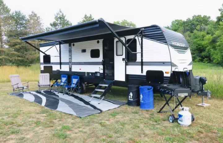 Spacious RV rental setup with extended awning, outdoor rug, camping chairs, and grill, perfect for a relaxing getaway.. Keystone Hideout 2022