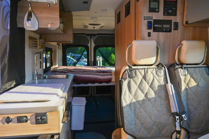This RV rental's interior features a compact kitchen with sink, cozy bed, & controls near passenger seats.. Winnebago Solis 59PX 2021
