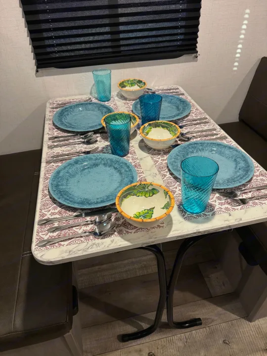 Cozy RV rental dining setup: a table set for four with blue plates and vibrant bowls, perfect for meals on the road.. Dutchmen Coleman 17B 2024