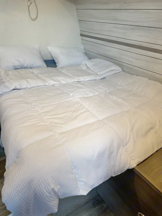 Cozy bed in an RV rental, with white bedding & wooden wall accents, perfect for a comfortable night.. Dutchmen Coleman 17B 2024