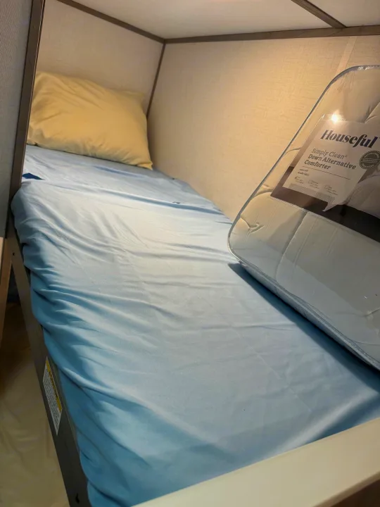 Cozy RV rental bunk bed with a fresh blue sheet, pillow, and new Houseful comforter, ready for a comfortable night's sleep.. Dutchmen Coleman 17B 2024