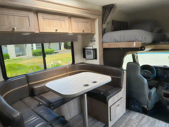 Spacious RV rental interior with a dining booth, overhead cabinets, and a comfortable cab-over bunk bed. Ideal for travel.. Forester Forester Motorhome 2019