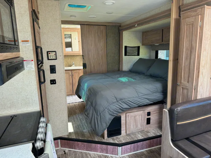 Step inside this RV rental showcasing a cozy bedroom with gray comforter, compact kitchen, and rear bathroom.. Forester Forester Motorhome 2019
