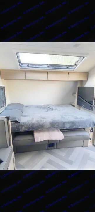 Cozy RV rental bedroom with comfy bed, skylight, overhead storage, and TV. Herringbone floor accents this travel trailer.. Ember Overland 2023