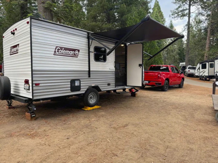 A Coleman travel trailer RV rental, with a red truck, set up for camping in a wooded campground.. Coleman Lantern LT 17B 2024