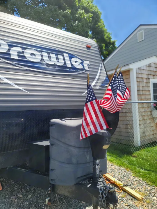 Sunny day for an RV rental. A Prowler travel trailer proudly displays American flags, parked on gravel.. Heartland RVs Prowler 2018
