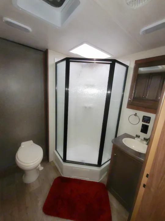 Interior of an RV rental bathroom with a corner shower, toilet, vanity, and wood flooring, perfect for your travels.. Heartland RVs Prowler 2018