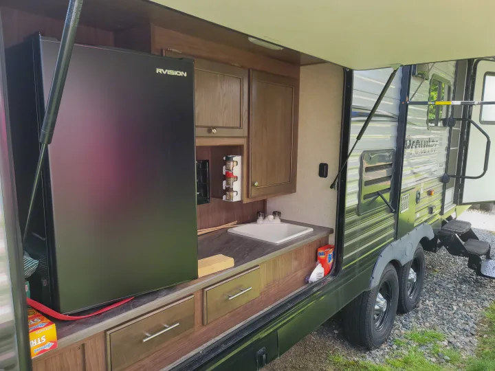 Experience camping convenience with this RV rental's outdoor kitchen, featuring a mini-fridge, sink, and cabinets under the awning.. Heartland RVs Prowler 2018