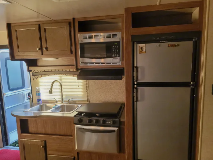 RV rental kitchen: Compact interior with sink, stove, microwave, and Dometic refrigerator, ready for your trips.. Heartland RVs Prowler 2018