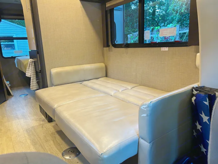 RV rental interior features a beige convertible sofa/bed, compact living space, and window with an 'EXIT' sign.. Thor Gemini 2017